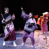 Theaterszene mit drei Akteuren in lilafarbenem Bühnenlich
