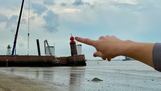 Eine Frau tippt scheinbar eine Turmspitze mit dem Finger an.