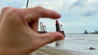 Zwei Finger halten scheinbar einen Turm fest.