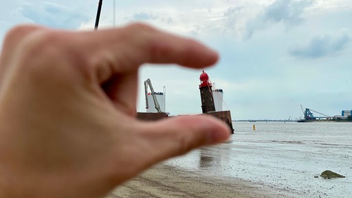 Zwei Finger halten scheinbar einen Turm fest.