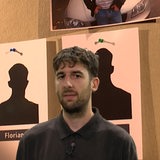 Ein Mann steht vor einer Pinnwand und schaut in die Kamera