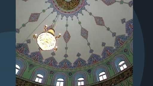 Eine gefließte Kupperl einer Moschee, von der ein Kronleuchter hängt