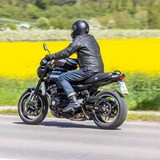 Motorradfahrer fährt auf einer Landstraße an einem blühenden Rapsfeld vorbei (Symbolbild).