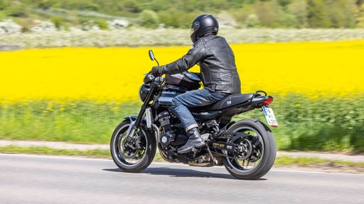 Motorradfahrer fährt auf einer Landstraße an einem blühenden Rapsfeld vorbei (Symbolbild).