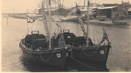 Auf einem Schwarz-Weiß-Bild sind zwei Boote auf dem Wasser zu sehen.