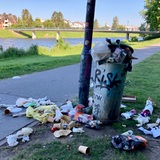 Ein Mülleimer am Werdersee ist überfüllt. Um den Mülleimer liegen mehre Plastiktüten, Pappbecher udn weiterer Müll. 