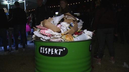 Ein Mülleimer mit der Aufschrift "Respekt" vollgefüllt mit Essen, Zigarettenschachteln und Pappe. 