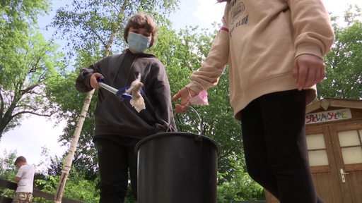 Zwei Schülerinnen, die Müll in einen Eimer werfen.