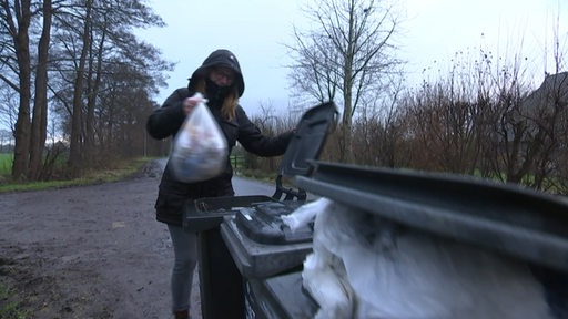 Eine Frau steckt ihren Plastikmüllbeutel in eine große Mülltonne, die am Straßenrand in Timmersloh steht.