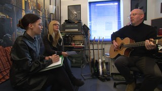 Drei Personen sitzen in einem Tonstudio und nehmen gemeinsam einen Song auf.