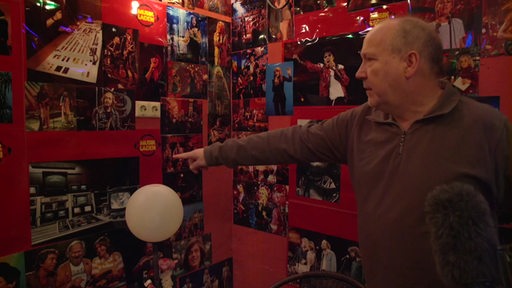 Ein Mann steht vor einer Wand mit vielen Bildern darauf und zeigt auf eins mit Pop-Legende Michael Jackson.