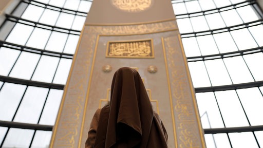 Eine muslimische Frau mit einem Khimar steht in der Kölner Moschee und blickts nach oben. 
