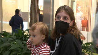 Eine Mutter mit Mund-Nasenschutz trägt ihr Kind auf dem Arm.