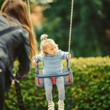 Eine Mutter schaukelt ihr Kind auf dem Spielplatz.