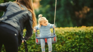 Eine Mutter schaukelt ihr Kind auf dem Spielplatz.