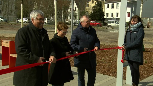 Drei Personen durchschneiden ein Band zur Einweihung eines Promenadenabschnitts.