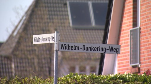 Ein Straßenschild über einer Hecke.