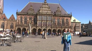 Zwei Touristen stehen auf dem Bremer Marktplatz und machen ein Selfie.