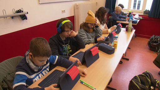 Schülerinnen und Schüler sitzen mit Tablets im Unterricht. 
