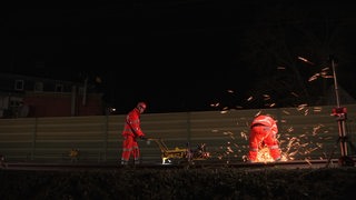 Arbeiter schweißen nachts an Bahngleisen