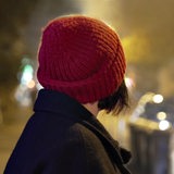 Rückansicht einer Frau mit Mütze, die nachts auf die Straße blickt.