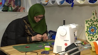 Eine Frau mit Kopftuch arbietet an einer Nähmaschine.
