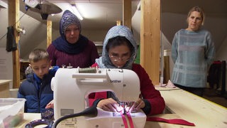 Zu sehen sind Migrantinnen, welche an einer Nähmaschine arbeiten.