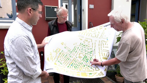3 Personen diskutieren über einem Lageplan das Ausbaunetz für Nahwärme in Bremen