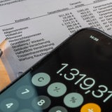 Ein Smartphone mit geöffneter Taschenrechner-App liegt auf einer Nebenkostenabrechnung.