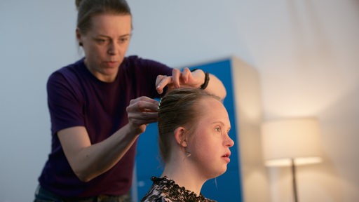 Maskenbildnerin richtet Haare einer jungen Frau mit Trisomie 21