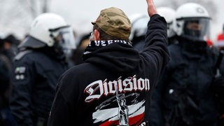 Ein Demonstrant auf einer Hooligan-Veranstaltung skandiert etwas vor einer Gruppe Polizisten.