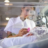 Eine Krankenschwester füttert ein Baby im Brutkasten mit einem Fläschchen.