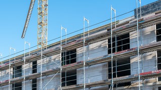 Der Rohbau eines Mehrfamilienhaus inklusive Gerüst und Kran.