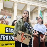 Luisa Neubauer mit einem Schild "Bohrkum", im Hintergrund Demonstranten und der niedersächsische Landtag