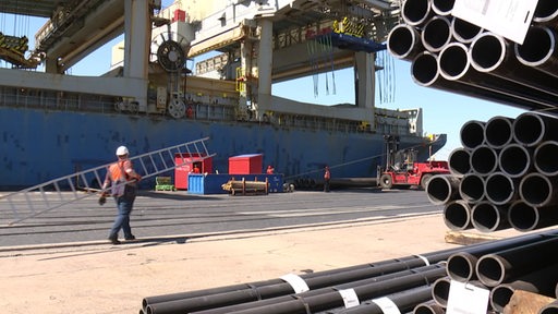 Ein Arbeiter, der mit einer Leiter am Neustädter Hafen entlanggeht, an der Seite sind mehrere Rohre zu sehen.