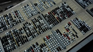 Blick aus der Luft auf hunderte Neuwagen auf einem Parkplatz.