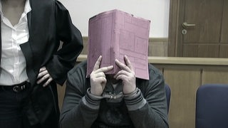 Der Patientenmörder Niels H. versteckt sein Gesicht hinter einer rosanen Aktenmappe