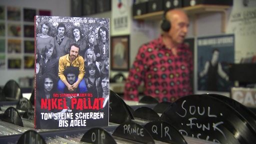 Der Bremer Nikel Pallat hört Musik im Plattenladen, rechts das Buch über sein Leben. 