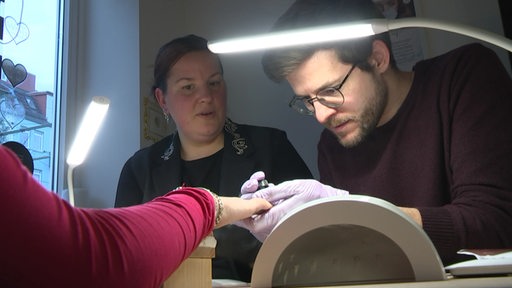 Niko Schleicher arbeitet an einem Nageldesign, neben ihm Alexandra Klier.