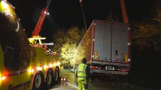 Ein Lastwagen wird von einem großen Fahrzeug mit einem Kran aus einer Böschung geborgen.