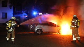 Zwei Feuerwehrleute löschen ein brennendes Auto.