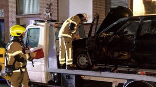 Feuerwehrleute löschen ein Auto, das auf einem Abschleppwagen steht.