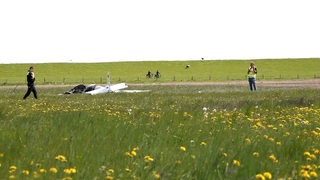 Zwei Polizisten neben dem Wrack eines Ultraleichtflugzeugs.