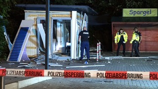 Ein Polizist steht vor einem zerstörten Container.