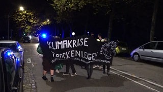 Mehrere Personen laufen mit einem Banner vor einem Blaulicht auf einer Straße.