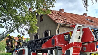 Vor einem Reihenendhaus steht ein Feuerwehrauto, Feuerwehrleute stehen in einem Korb einer Drehleiter.