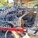Zwei abgebrannte Autos stehen auf einem Parkplatz unter einer Brücke in Bremen.