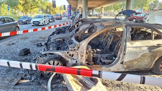 Zwei abgebrannte Autos stehen auf einem Parkplatz unter einer Brücke in Bremen.