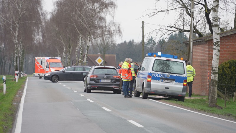 Polizisten stehen neben mehreren Autos auf einer Landstraße