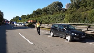Ein beschädigtes Auto steht auf einer Autobahn. Ein Polizist läuft über die gesperrte Fahrbahn.